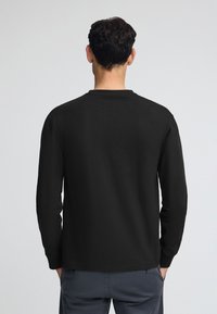 Svart långärmad t-shirt med rund halsringning. Gjord av mjukt, lätt tyg, med en standardpassform och utan synligt märke eller mönster.