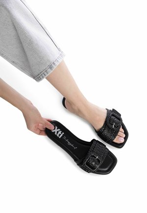Sandali a scivolo neri in tessuto intrecciato con punta quadrata, caratterizzati da una grande fibbia decorativa. Parte superiore testurizzata e suola piatta per il massimo comfort.