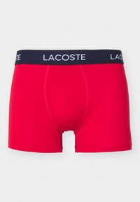 Piros boxer alsónadrág rugalmas anyagból, sötétkék elasztikus derékkal, amelyen fehér "LACOSTE" felirat található, és ívelt szabású.