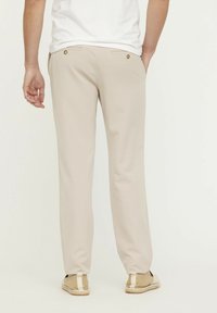 Pantalons légers beiges à coupe droite. Comprend deux poches arrière avec boutons, associés à des espadrilles de couleur claire.