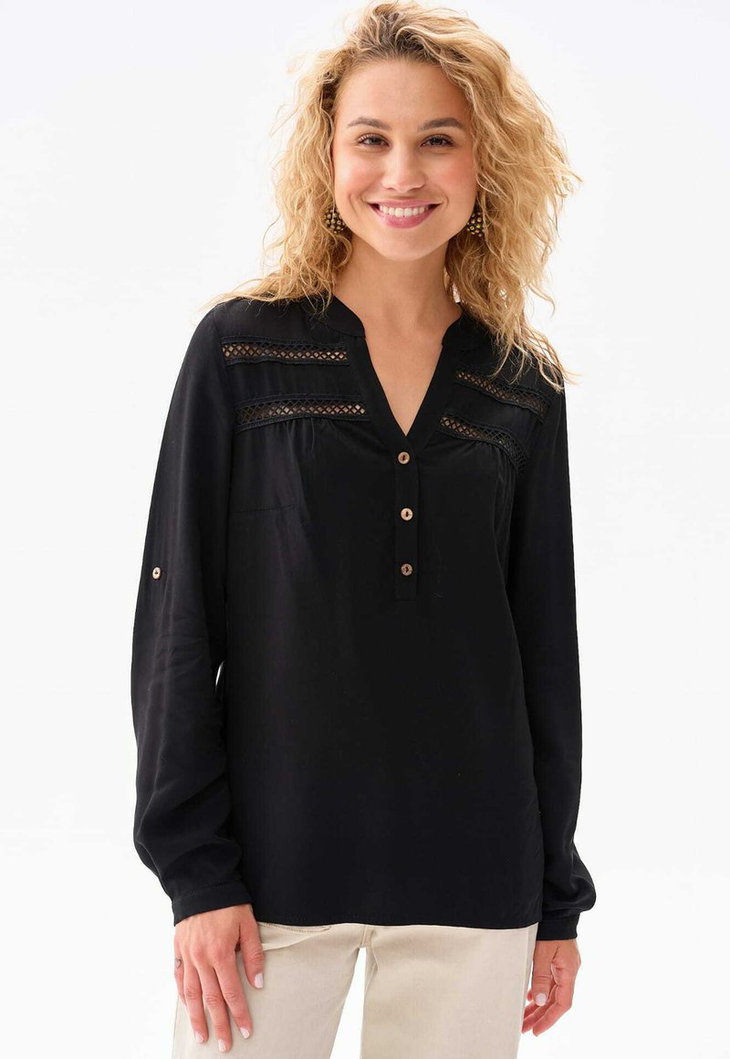 Schwarze Bluse mit langen Ärmeln und V-Ausschnitt, mit strukturierten Einsätzen und dekorativen Knöpfen. Aus leichtem Stoff gefertigt, hat sie einen lockeren Schnitt.