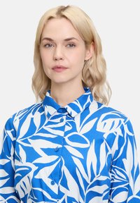 Camicia button-up blu e bianca con motivo a foglie, colletto classico e tessuto di cotone liscio con una leggera finitura lucida.