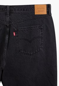 Černé džínové kalhoty z denimu s kapsou na zadní straně, která má zakřivený šev, a opalovací koženou štítkem s nápisem "Levi Strauss & Co."