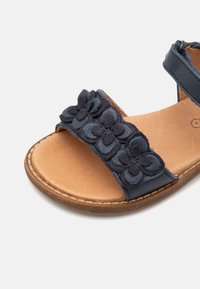 Sandale marine avec des accents en daim floral, des sangles en cuir et une semelle rembourrée marron clair. Comprend deux larges sangles pour un soutien optimal.