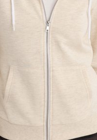 Felpa zip-up beige realizzata in morbido tessuto, con zip frontale, due tasche anteriori e lacci bianchi regolabili sul cappuccio.