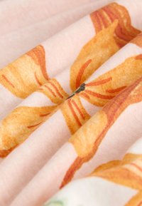 Mehka tkanina z vzorci oranžnih in rumenih cvetov na svetlo rožnati podlagi, prikazana z gubami in v prikazu od blizu.