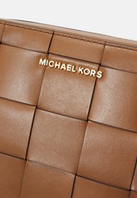 Sac à main en cuir tressé marron avec une surface subtilement texturée. Présente un logo "MICHAEL KORS" doré. Design compact avec une finition robuste.