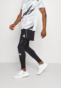 Czarne legginsy sportowe z białymi akcentami, w połączeniu z szaro-białą koszulą z krótkim rękawem w wzory oraz białymi trampkami.