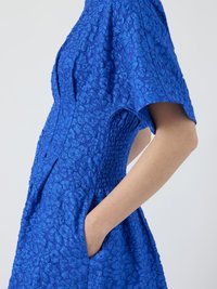 Blaues, strukturiertes Kleid mit floralem Muster, kurzen Ärmeln und seitlichen Taschen. Verfügt über ein tailliertes Oberteil mit Raffung.