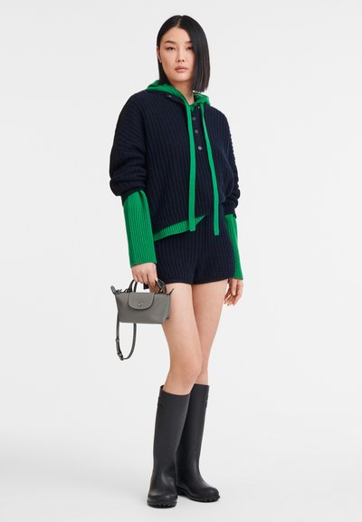 Navy and green knit hooded cardigan with buttons, paired with navy shorts. Model wears gray mini bag and black knee-high rubber boots.