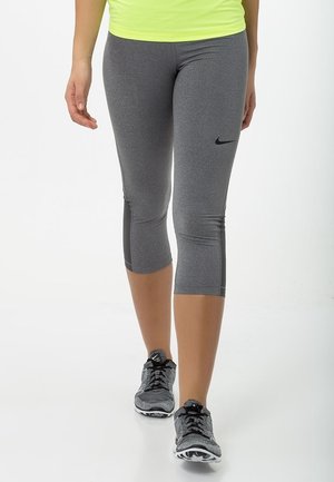 Person wearing gray Nike cropped leggings and gray-black Nike running shoes, walking against a plain white background.