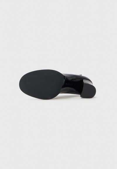 Escarpin en cuir noir avec une texture lisse, un bout arrondi et un talon carré. La semelle est plate et robuste avec un branding minimal.
