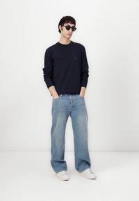 Navy sweatshirt, light blue wide-leg jeans, and white sneakers; accessorized with dark sunglasses; simple design, casual fit, minimal branding.