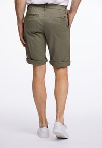 Olivgröna shorts visade bakifrån, med uppvikta fållar och två bakfickor. Bärs med vita sneakers. Slät tygtextur.