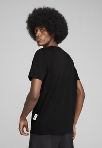 Sort t-shirt med korteærmer, rund halsudskæring og en glat tekstur; har diskrete brandlogoer på siden nær kanten.