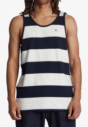 Mand iført ærmeløs tanktop med brede vandrette navyblå og hvide striber, stående foran en hvid baggrund.