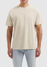 Beige katoenen t-shirt met korte mouwen en een ronde hals, gecombineerd met lichtblauwe jeans. Gladde textuur en basisontwerp.
