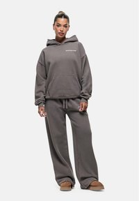 Felpa grigia over size con tasca frontale e cappuccio con lacci abbinata a pantaloni della tuta grigi e scarpe slip-on marroni.