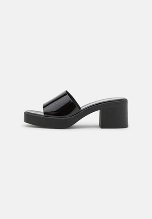 Sort sandal i lak med en tyk platformhæl. Glat overdel og tekstureret ydersål. Åben tåsandalsdesign med en elegant form.