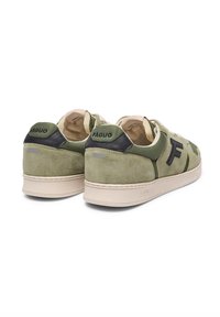 Grüne Wildleder-Sneaker mit schwarzen Akzenten, runden Schnürsenkeln und beige Gummisohlen. Strukturierte Überzüge und Logo-Detail an der Ferse.