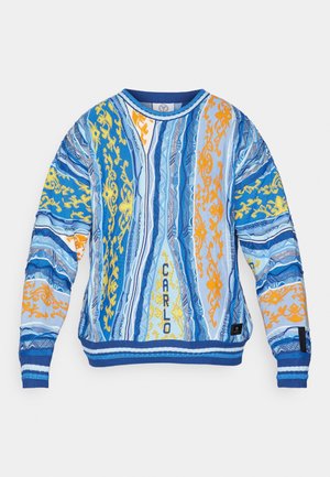 Pull à motifs bleus et blancs avec des dessins complexes jaunes et orange, col rond, poignets et ourlet côtelés, avec le texte "CARLO".