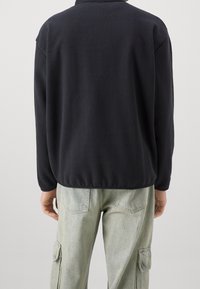 Fleecejacka i mörk marinblå, med krage och långa ärmar. Har en avslappnad passform och en mjuk, len textur för komfort.