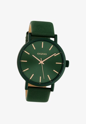Montre verte avec une finition mate, présentant des aiguilles et des marqueurs dorés minimalistes. Le bracelet vert doux complète le design du cadran rond.