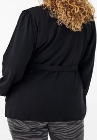 Blusa nera a maniche lunghe in tessuto texturizzato con cintura legata in vita, abbinata a pantaloni grigi a fantasia con stampa zebra.
