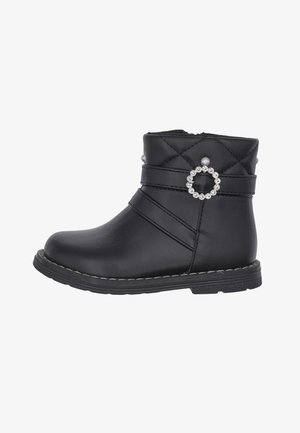 Bottine noire à cheville avec dessus matelassé, boucle ronde décorative en strass, accents de perles et semelle cousue sur fond blanc.