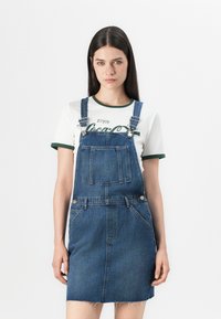 Denim üleri kleit reguleeritavate rihmadega, esiseguga ja narmastega heml. Kombineeritud valge T-särgiga, millel on rohelised aktsendid ja tekst.