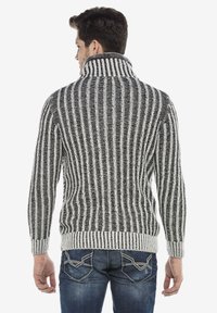 Gebreide coltrui in zwart en wit, met verticale strepen en een ribbelstructuur, afgewerkt met boorden en een zoom.