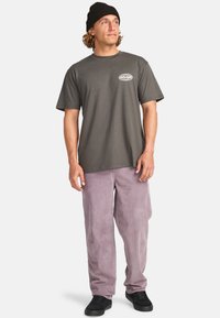 Gray cotton t-shirt with a round neckline and chest graphic, paired with light purple corduroy pants. Black sneakers complete the outfit.