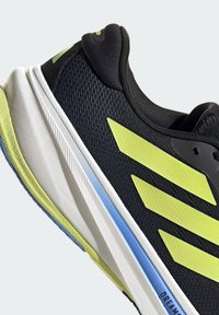 Zapato deportivo negro con rayas verde lima, parte superior texturizada, mediasuela blanca y acento azul en la suela. Detalle de collar de tela suave.
