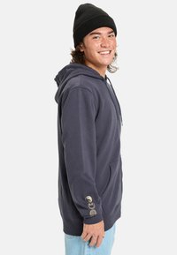 Navy hoodie made of fleece with a front pocket. Features a drawstring hood and gold graphic accents on the left sleeve.