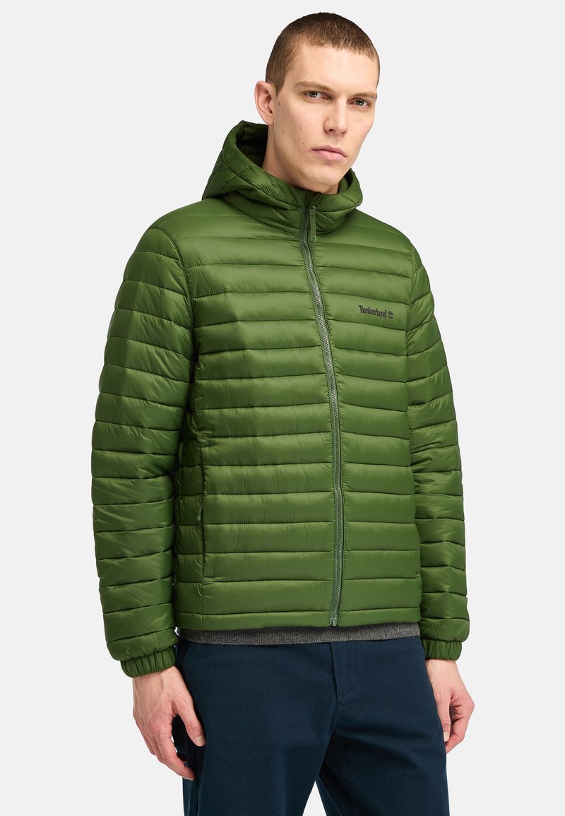 Groene gewatteerde jas met een kap, uitgerust met gestikte horizontale lijnen, een rits aan de voorkant en een klein logo op de linkerborst.
