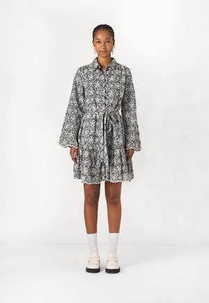 Svart og hvit blomstermønstret skjortekjole med innsnørt liv, lange belledeler og bølget nederkant. Brukt med hvite sokker og loafers.