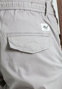 Pantalones cortos de color gris claro hechos de algodón, con una cintura elástica, que cuentan con un bolsillo trasero y una etiqueta blanca con el texto "Reel".