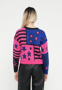 Strikket genser med rosa, blå og svarte seksjoner med stjerner og striper. Myk tekstur og avslappet passform, rund hals.