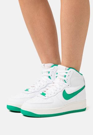 Baskets montantes blanches avec accents verts et logo Nike, en cuir texturé, col rembourré et semelle en caoutchouc. Fermeture à lacets.