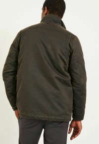 Dunkelgrüne, strukturierte Jacke mit Stehkragen. Verfügt über sichtbare Nähte und einen lässigen Schnitt. Kann Taschen und einen leicht abgetragenen Look enthalten.
