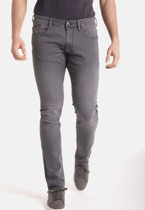 Jean en denim gris slim-fit avec cinq poches, fermeture bouton et décoloration subtile. Associé à des baskets grises pour un look complet.