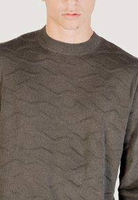 Grauer Strickpullover mit Wellenmuster, Rundhalsausschnitt und weicher Textur, der den lässigen Schnitt und das detaillierte Design betont.