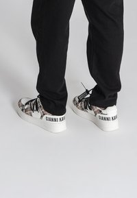 Bílé a hnědé sneakers s vzorem a černými šněrovadly, s logem "GIANNI KAVAKI" na patě a texturovanou bílou podrážkou.