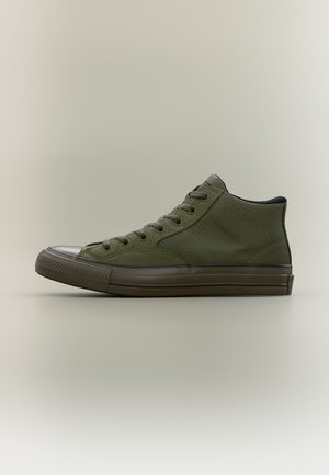 Υφασμάτινο παπούτσι τύπου sneaker υψηλού λαιμού σε ελιάς πράσινο με μαύρη λαστιχένια σόλα και προστατευτικό καπάκι στα δάχτυλα, σε ουδέτερο φόντο, από πλευρική όψη.