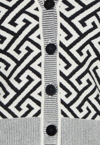Zwart-wit cardigan met een geometrisch patroon, zwarte knopen en een geribbelde grijze zoom. Zachte gebreide textuur.