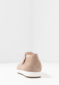 Zapato de ante beige con punta redonda, suela blanca y un detalle de corte lateral. Textura suave con diseño minimalista.