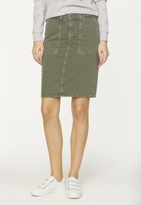 Jupe en denim vert olive avec poches avant, fermeture à bouton et à glissière, longueur genou et texture délavée, associée à des baskets blanches.