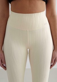 Leggings taille haute en crème avec un design côtelé texturé comportant des lignes verticales et un petit logo sur la taille.