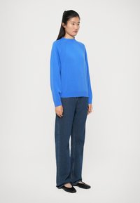 Blå strikkegenser med lange ermer, rund hals og avslappet passform, kombinert med mørkeblå rette jeans og svarte leiligheter.