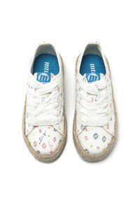 Zapatillas de lona blancas con estampados florales multicolores, que cuentan con una suela de cuerda de yute y cordones blancos. Plantillas azules visibles en el interior.